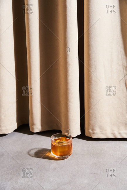 Cocktail with large ice cubes by beige drapes