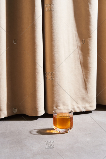 A cocktail with large ice cubes by beige drapes