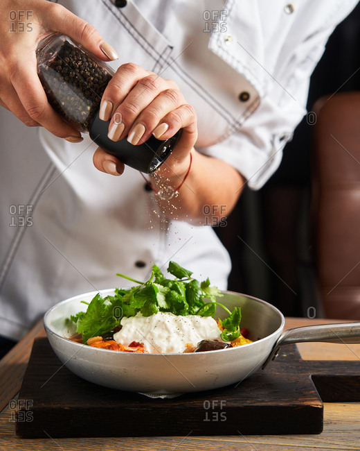 Chef topping a gourmet dish with fresh ground pepper in a frying pan
