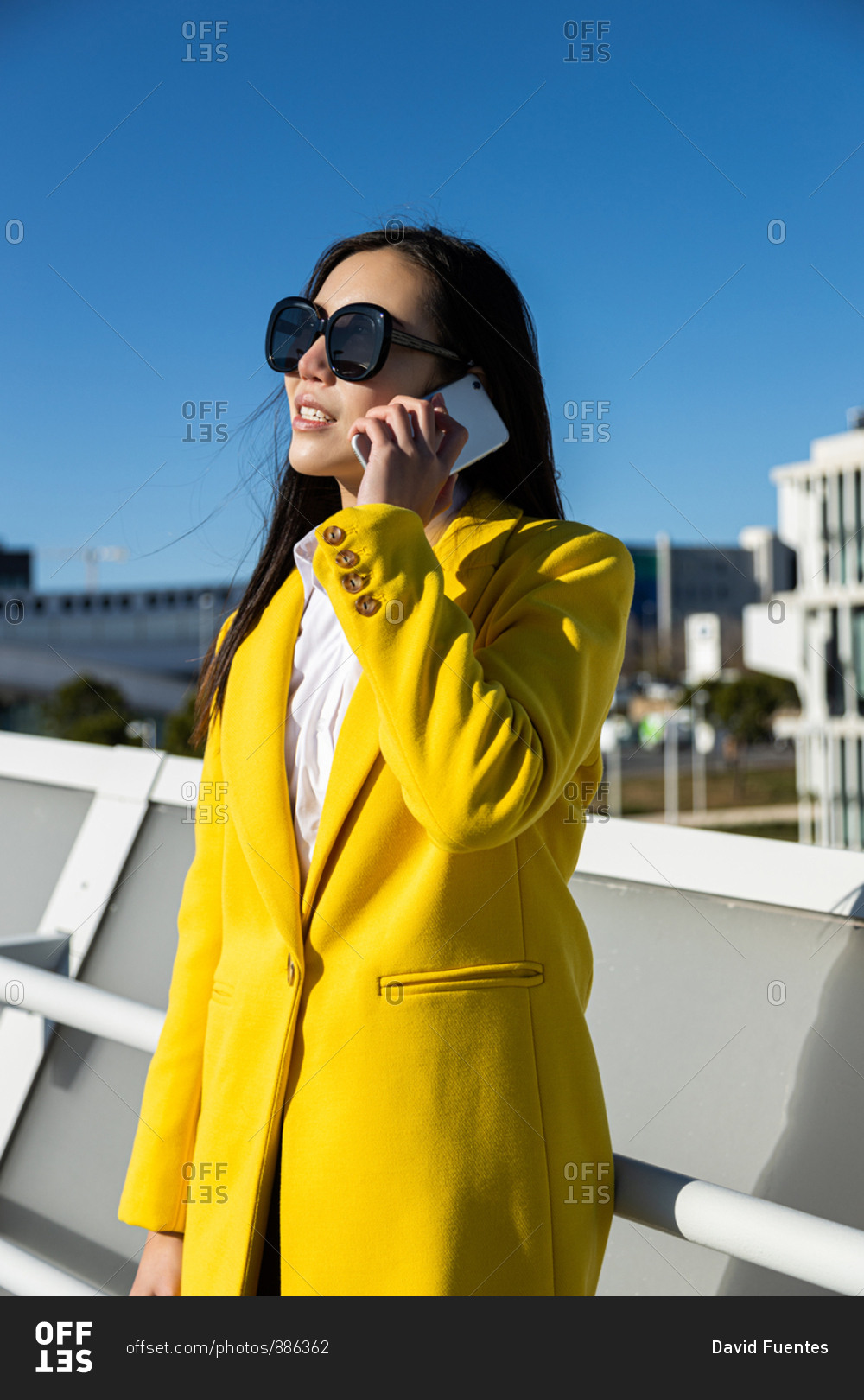 Asian business woman with yellow coat talking on phone with city in the background