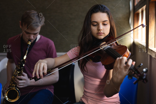 Front view of a Caucasian teenage male and female musician rehearsing, the girl playing the violin and the boy playing the saxophone
