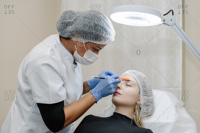 Beautician performs a corrector treatment of eyebrows on a young woman