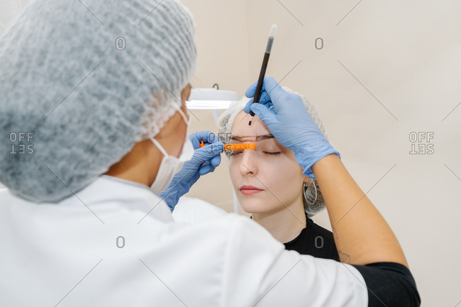 Esthetician performs a corrector treatment of eyebrows on a young woman