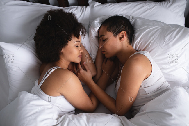 High angle close up view of a mixed race female couple at home in the bedroom, lying asleep in bed together in the morning, facing each other
