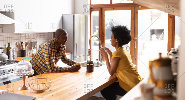 Side view of an African American couple at home in the kitchen, sitting on either side of the kitchen island, drinking coffee and talking