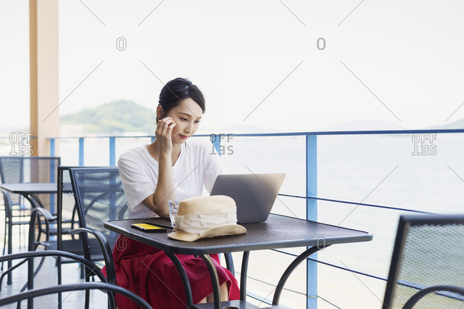 Female Japanese professional sitting on balcony of a co-working space, using laptop computer.