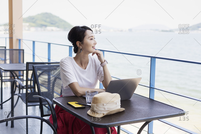 Female Japanese professional sitting on balcony of a co-working space, using laptop computer.