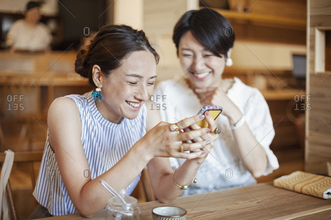 Two Japanese women sitting at a table in a vegetarian cafe, using mobile phone.