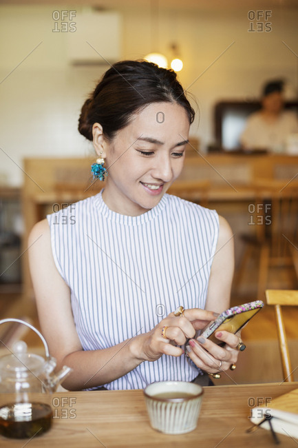 Japanese woman sitting at a table in a vegetarian cafe, using mobile phone.