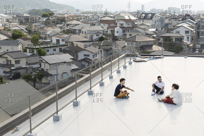 High angle view of group of young Japanese men and women sitting on a rooftop in an urban setting.