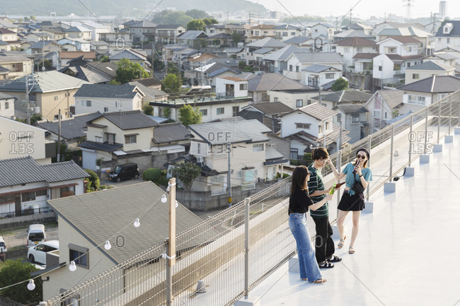 High angle view of group of young Japanese men and women standing on a rooftop in an urban setting.
