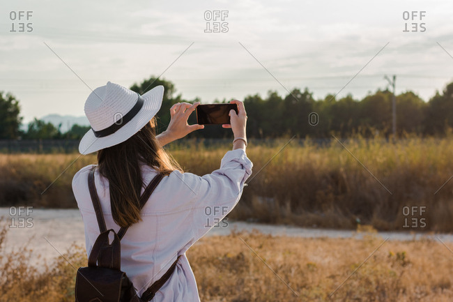 Young woman is taking a picture with her smartphone in a field. Adventure, technology