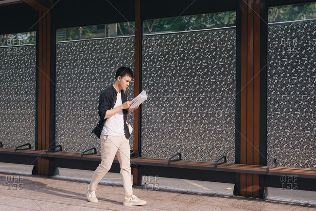 Serious man in casual wear reading book while walking at urban setting in city area