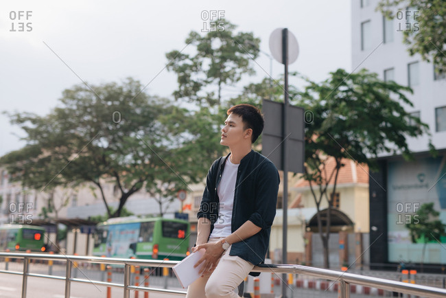 Young man waiting at bus stop, leaning on a railing in the middle of the street