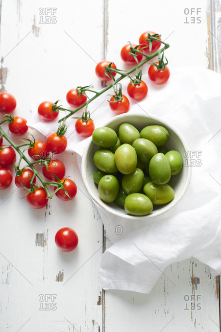 Cherry tomatoes and green whole olives on white wooden table. Cooking fresh salad