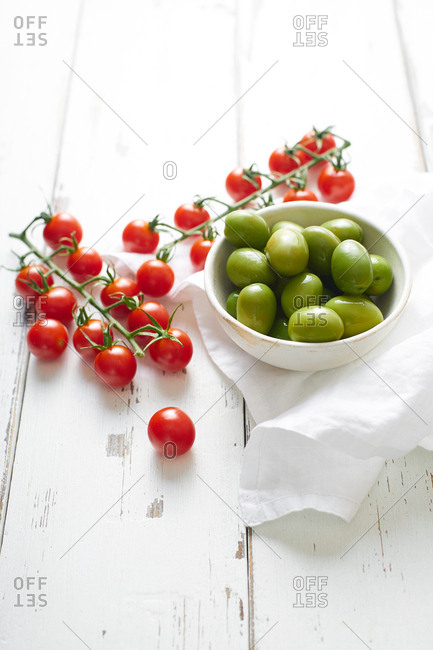 Cherry tomatoes and green whole olives on white wooden table.