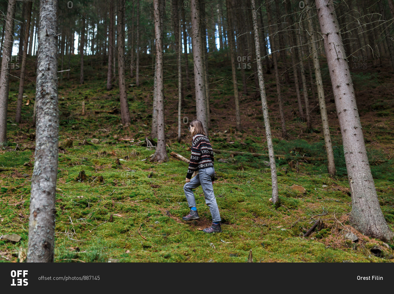 The young woman in the cozy sweater is hiking in the forest and enjoying the landscape