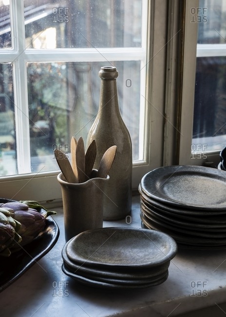 Stoneware plates and wooden utensils on counter by artichokes