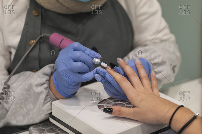 Technician using electric buffer on woman's nails during manicure
