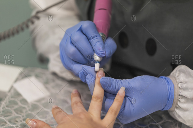 Close up of technician using electric file on woman's nails during manicure