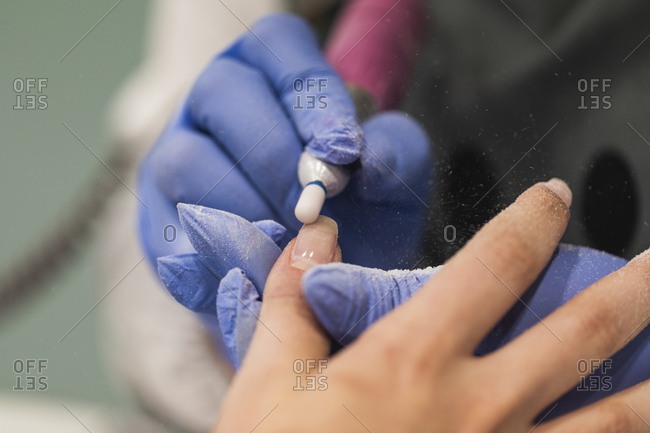 Close up of a nail tech using electric file on woman's nails during manicure