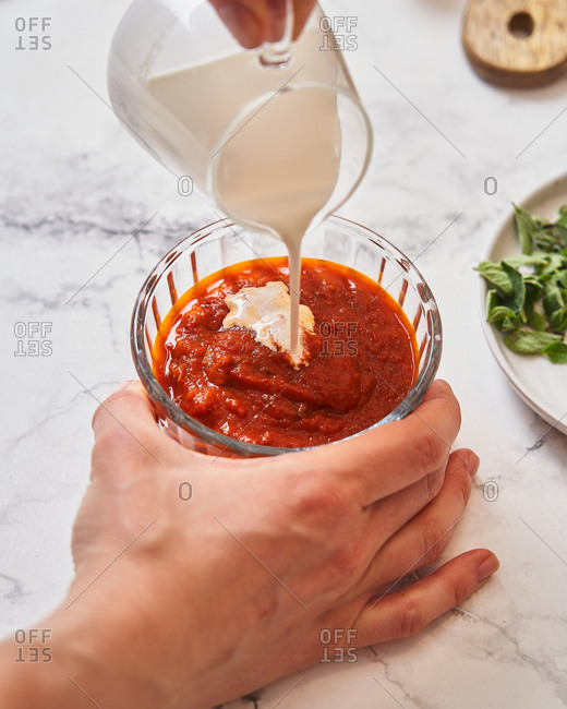 Chef pouring cream into sauce on marble surface