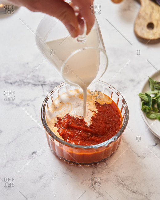 Person pouring cream into sauce on marble surface