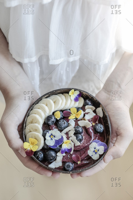 Midsection of girl holding ice cream garnished with fruits and edible flowers in bowl at home