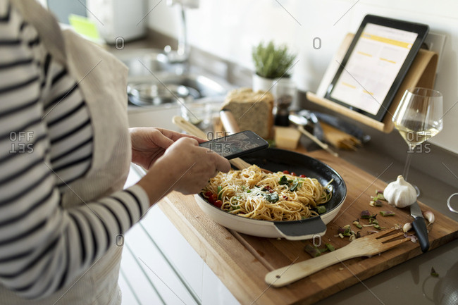 Close-up of woman taking smartphone picture of her pasta dish in kitchen at home
