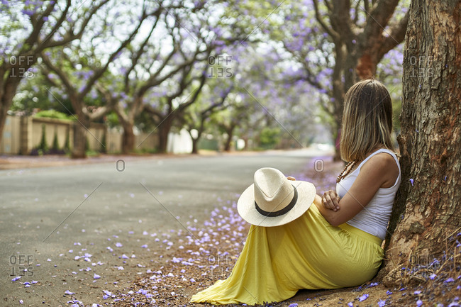 Woman leaning on a tree at a street with jacaranda trees in bloom- Pretoria- South Africa