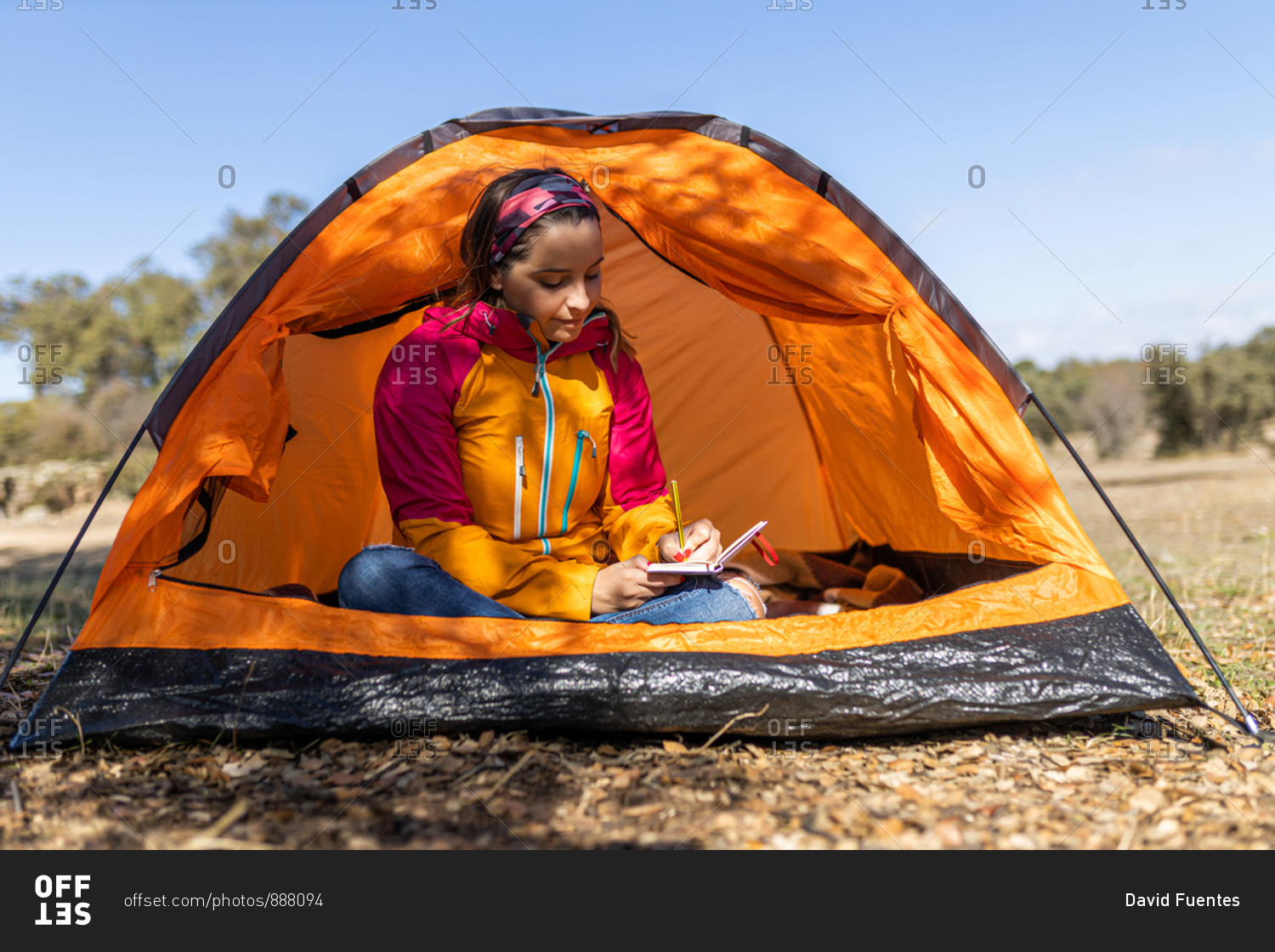 Young camping woman sitting in her tent, writing in her notebook