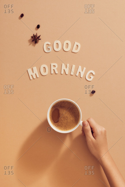 Hand holding cup of coffee under Good Morning sign