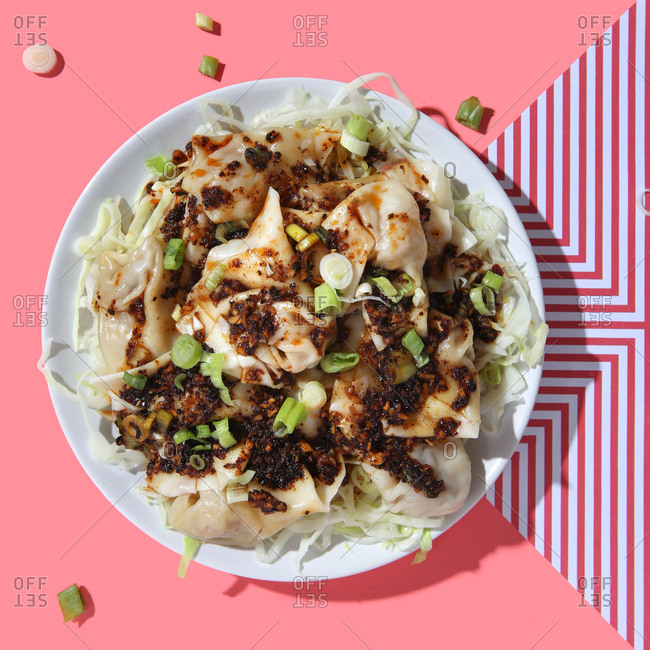 Szechuan wontons plated on bright background.