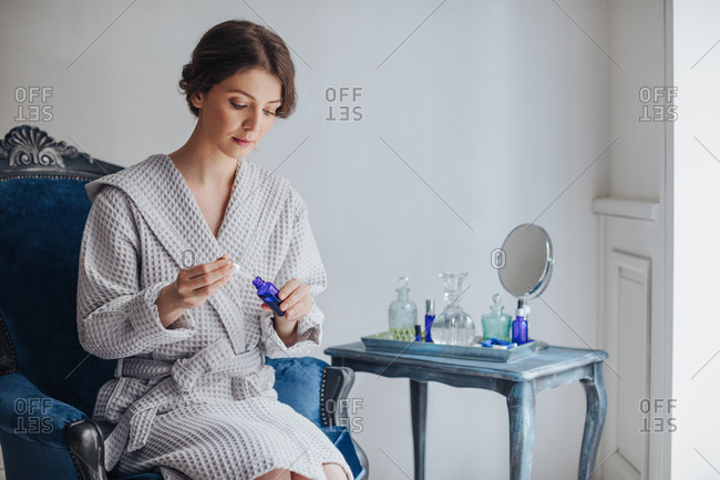 Beautiful Caucasian woman in bathrobe sitting at luxury spa salon and  holding cosmetic serum bottle.
