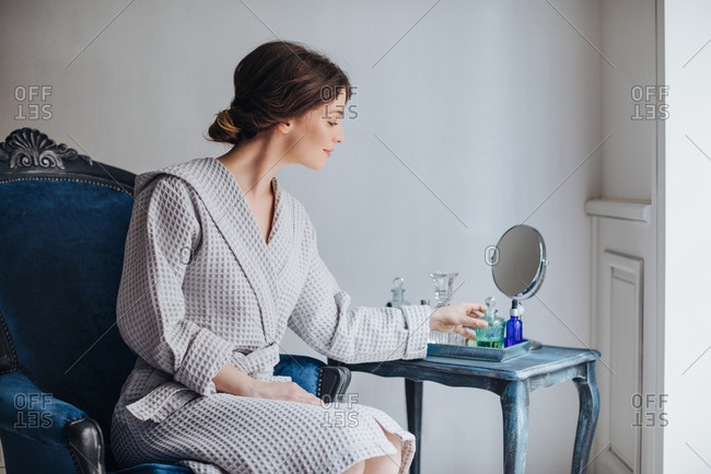 Beautiful Caucasian woman in bathrobe sitting at luxury spa salon and  holding cosmetic serum bottle.