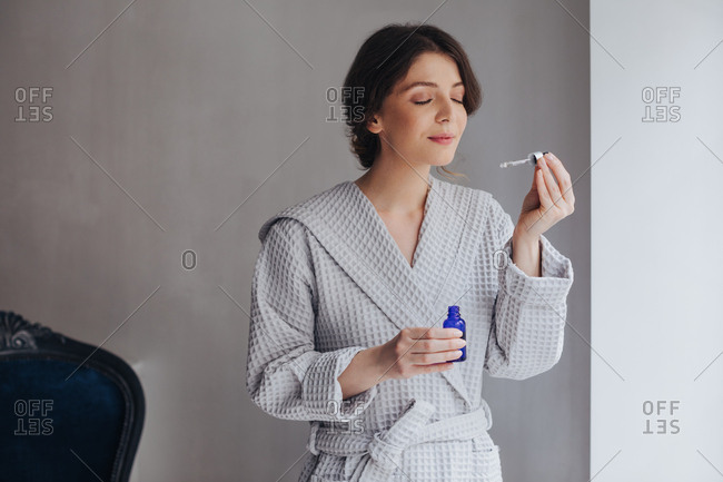 Beautiful Caucasian young woman holding cosmetic serum and smelling pipette.