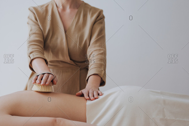 Hand of unrecognizable woman masseuse doing massage with brush on woman's back.