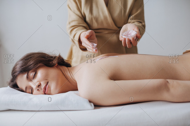 A masseuse putting natural moisturizing cosmetic cream on woman's back at spa salon.