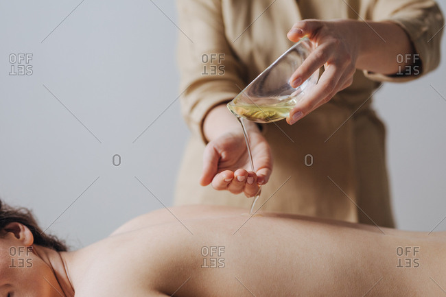 Hands of unrecognizable woman masseuse pouring massage oil on woman's back.