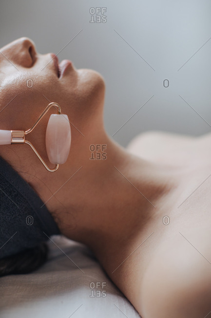 Unrecognizable cropped woman enjoying face massage with crystal roller at spa salon.