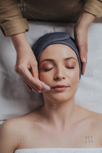 Beautiful young woman enjoying crystal face massage at spa salon.