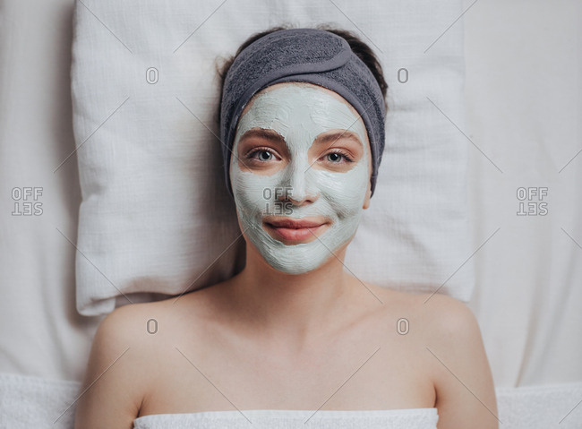 Portrait of pretty Caucasian woman laying at spa salon with cosmetic mask on her face and looking at camera.