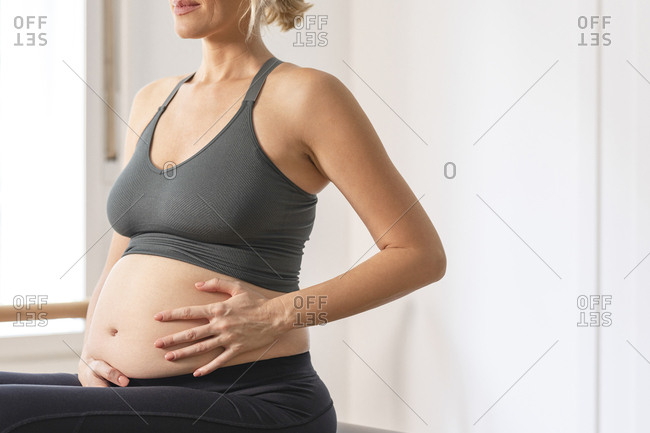 Anonymous pregnant woman in sportswear holding her hands on her pregnant belly.