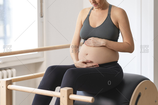 Anonymous pregnant woman in sportswear holding her hands on her pregnant belly.