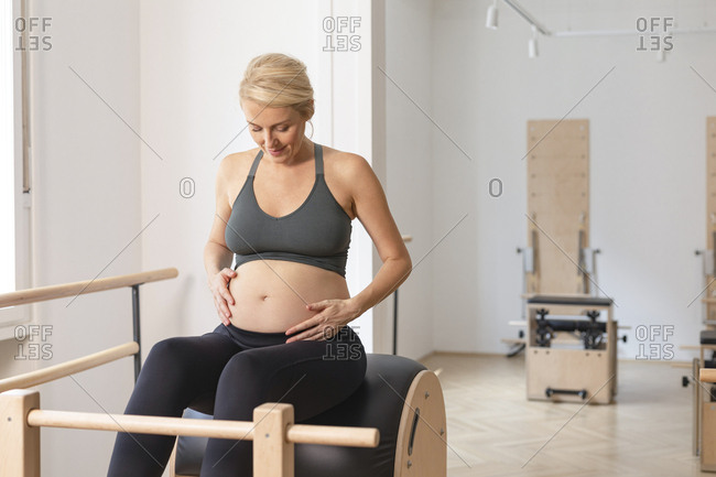 Portrait of beautiful blonde pregnant smiling woman in sportswear holding her hands on her pregnant belly.