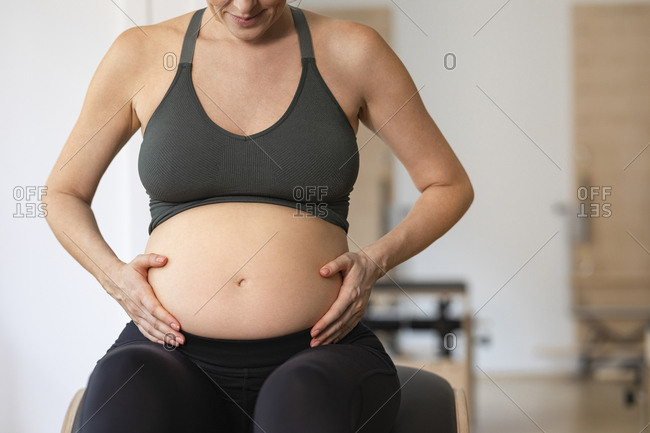 Anonymous pregnant woman in sportswear holding her hands on her pregnancy belly.