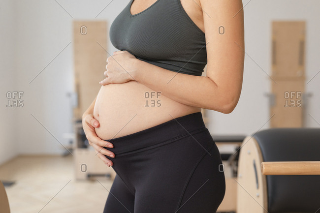 Unrecognizable pregnant woman in sportswear holding her hands on her pregnancy belly.