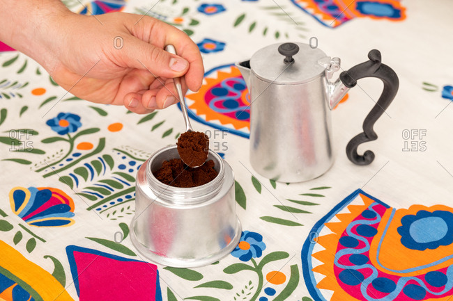 Hand filling a moka pot with coffee grounds on a colorful background