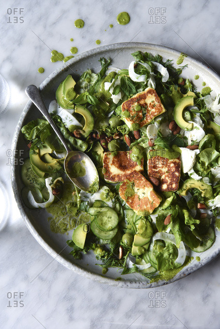 Green Salad with halloumi and dressing in a ceramic bowl.