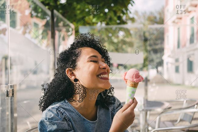 Carefree, excited young woman enjoying pink ice cream cone on sunny cafe patio